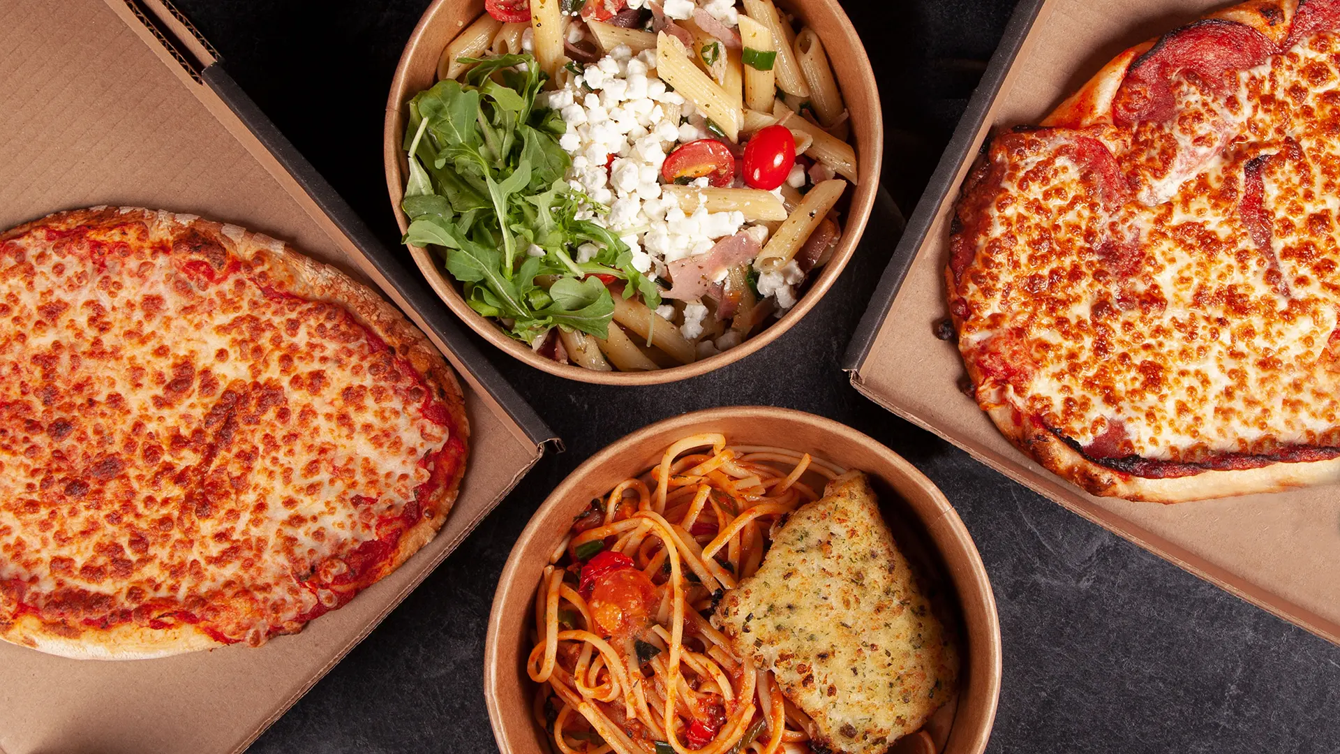 Offre familiale de PACINI comprenant pizzas, pâtes, salade et pain à l’ail préparés pour emporter ou en livraison.